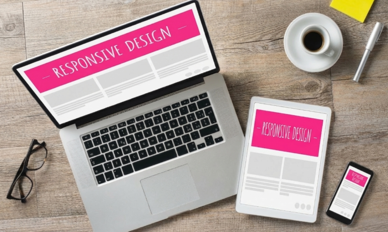 A flat lay photograph of a laptop, tablet, and smartphone on a wooden desk. All three screens display a "RESPONSIVE DESIGN" wireframe mockup, demonstrating how a website layout adapts to different device sizes.